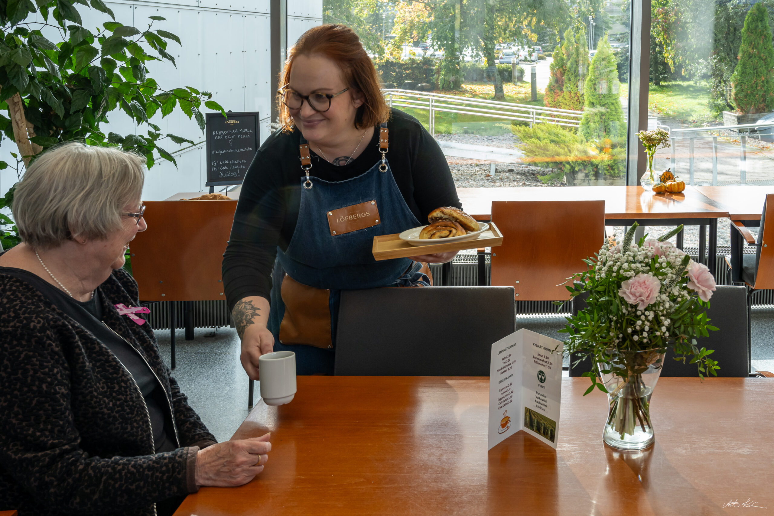 Nainen tarjoilee asiakkaalle kahvia ja ruokaa pöyään