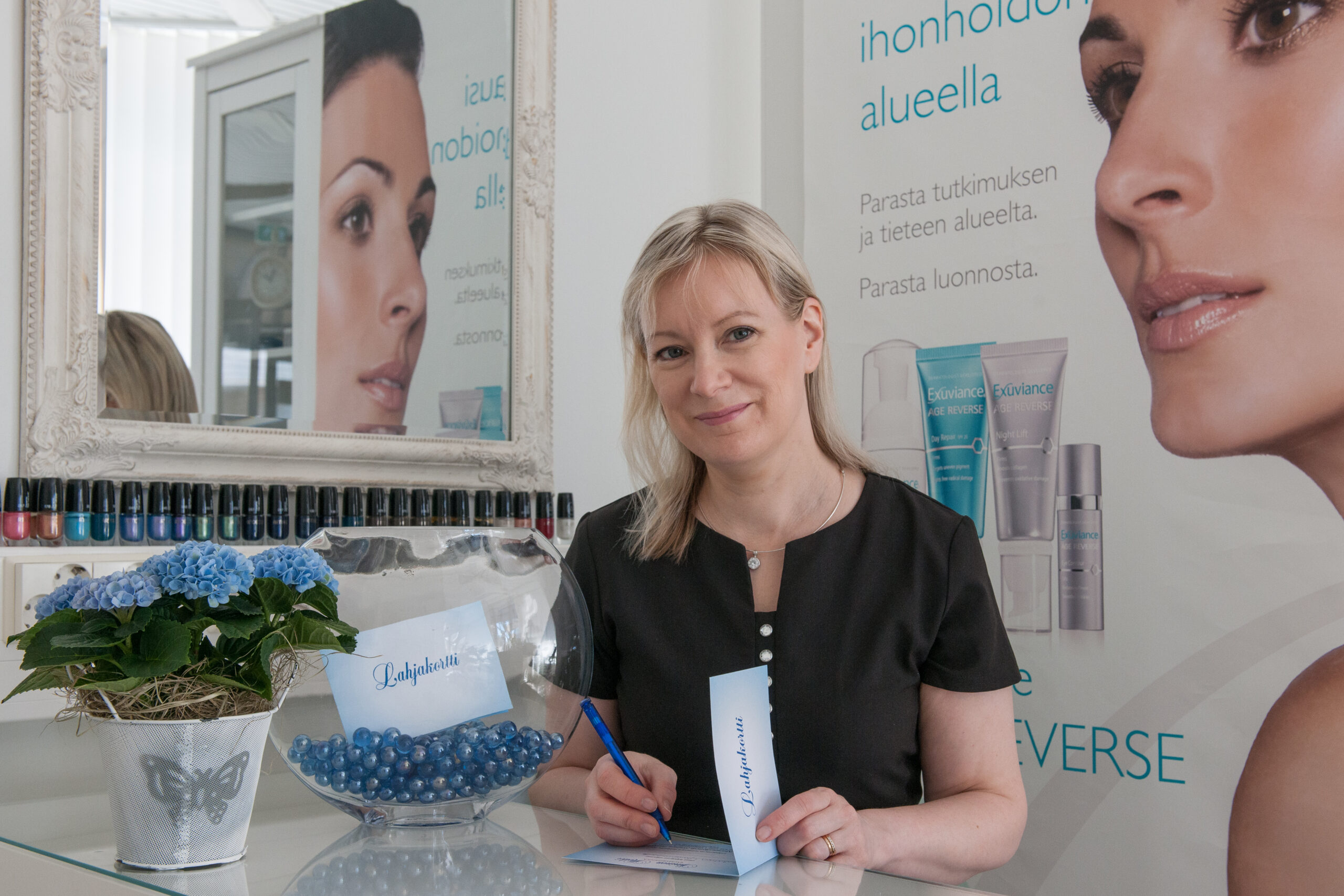 Hoitolassa työskentelevä nainen istuu pöydän ääressä ja kirjoittaa lahjakorttia hymyillen